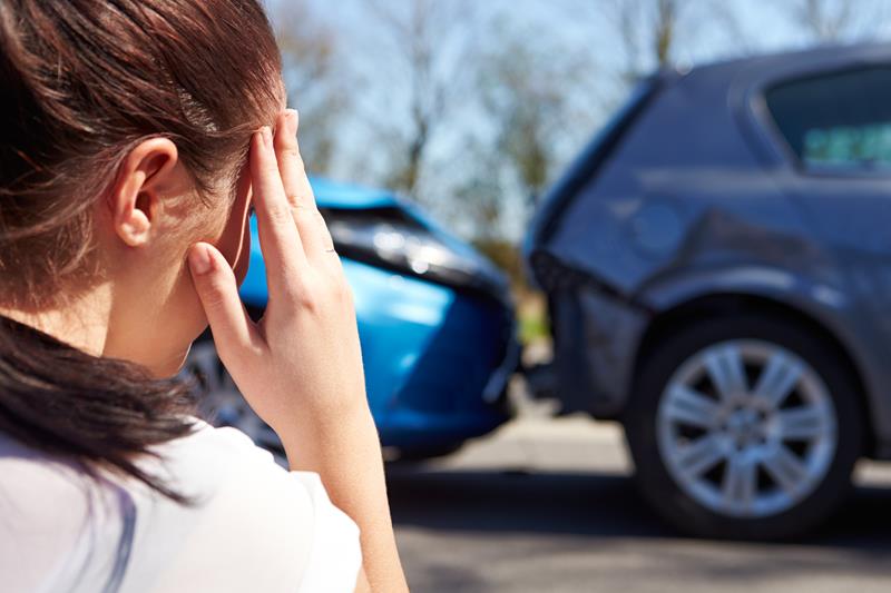 Woman holding her head at the roadside after a car accident, damaged cars behind her