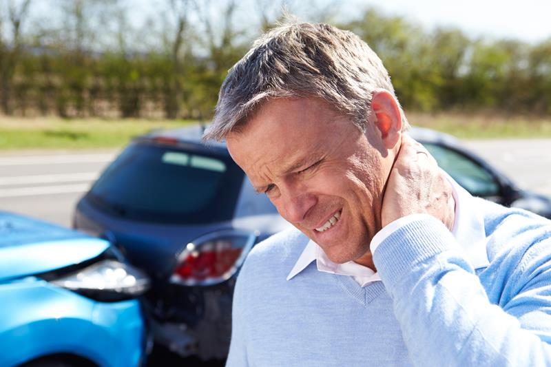 Man holding his neck in pain beside two cars after a collision